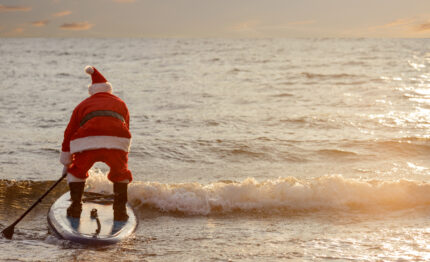 Man in Santa costume with SUP board on winter sea