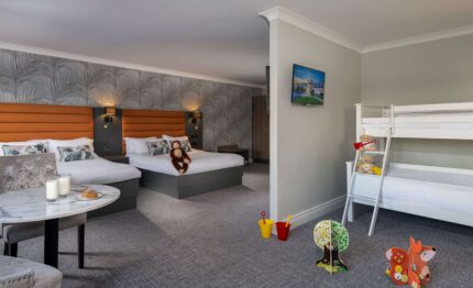 Spacious family hotel room with cosy double beds, children's bunk beds, toys, stylish decor, and a welcoming atmosphere.