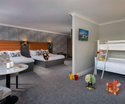 Spacious family hotel room with cosy double beds, children's bunk beds, toys, stylish decor, and a welcoming atmosphere.