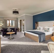 Spacious hotel suite with cosy king-size bed, elegant sofa, flat-screen TV, and vibrant flowers, offering a relaxing stay.