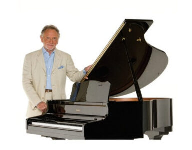 Smartly dressed elderly gentleman beside grand piano in elegant hotel lobby; enjoy live music and sophisticated ambiance.