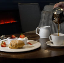 Indulgent afternoon tea with scones and fresh strawberries in a cosy hotel lounge with a warm fireplace ambiance.