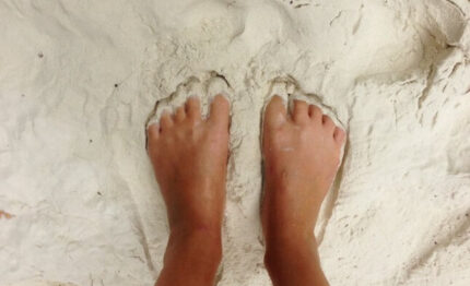 Bare feet gently sinking into soft, white sandy beach, evoking relaxation at beachfront hotel getaway.