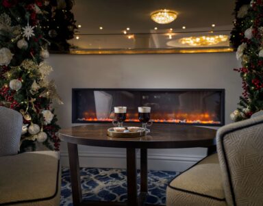 Cosy hotel lounge with festive decor and warm fireplace, perfect for relaxation and enjoying hot drinks.