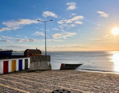 Stunning seaside view with vibrant beach huts, sunlit sea, and boats, perfect for a serene coastal getaway.