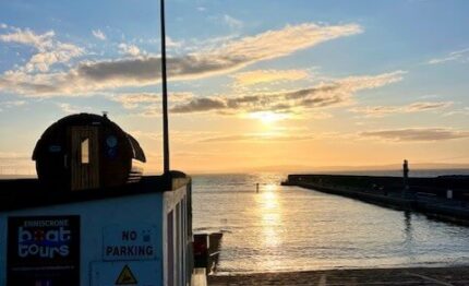 Stunning sunset over serene harbour with boat tours and cobblestone path; ideal for relaxing coastal holiday.