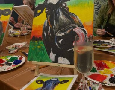 Guests enjoy painting a cow at a lively art class in the hotel; vibrant colours and champagne enhance the creative experience.