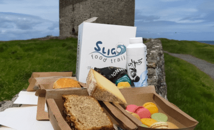 Guests enjoy scenic picnic with cheese, bread, macarons, and drinks near historic stone tower on Sligo Food Trail.
