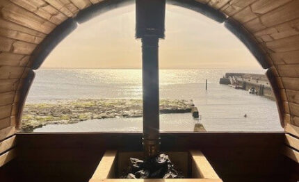 Cosy wooden sauna with sea view, warm sunlight, and scenic waterfront, offering a relaxing retreat experience for guests.
