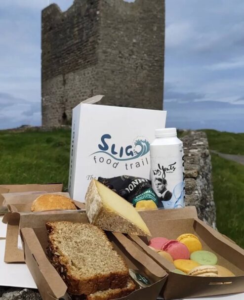 Picnic with local treats in front of Sligo castle ruins, showcasing colourful macarons, gourmet cheese, and fresh bread.