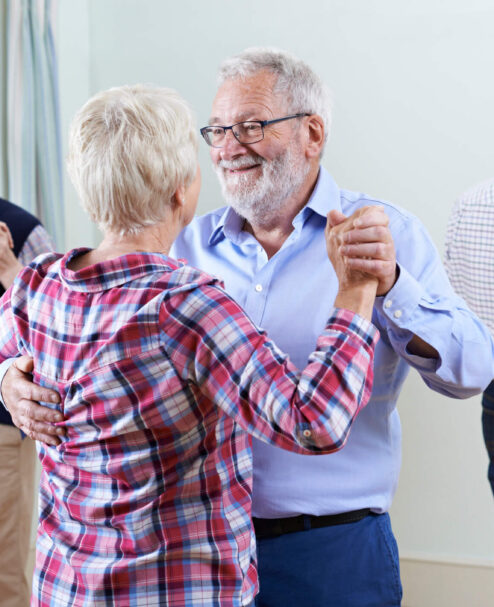 Elderly couples joyfully dancing in spacious hotel lounge with bright windows and serene atmosphere.