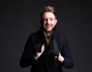 Smiling guest in smart dark jacket holding a loosened black tie in a stylish hotel lobby setting, welcoming concierge and boutique comforts