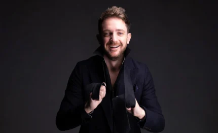 Smiling guest in smart dark jacket holding a loosened black tie in a stylish hotel lobby setting, welcoming concierge and boutique comforts