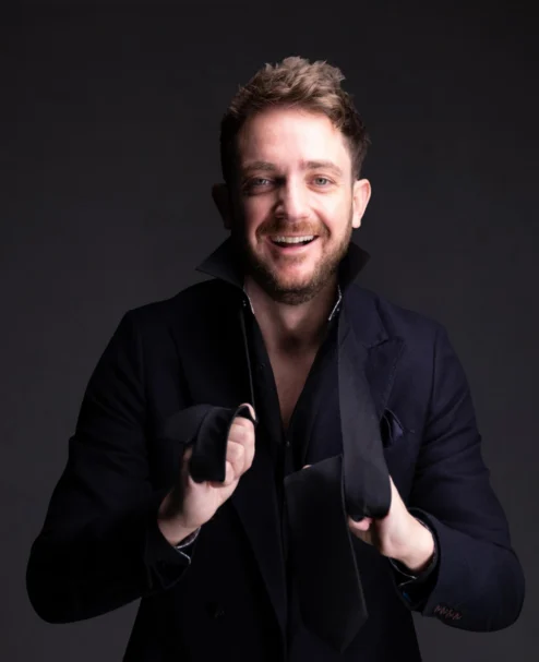 Smiling guest in smart dark jacket holding a loosened black tie in a stylish hotel lobby setting, welcoming concierge and boutique comforts